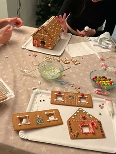 three people making gingerbread houses at a table with candy and candies in front of them