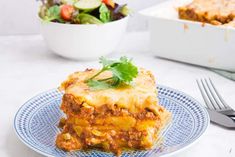 a blue plate topped with lasagna next to a white bowl filled with salad