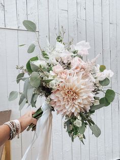 a bouquet of flowers is being held up by someone's hand with a white ribbon