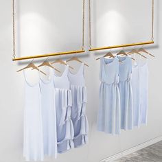 three white dresses hanging on clothes racks in front of a mirror with gold bar handles