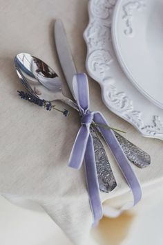 a table with silverware and lavender ribbon on it