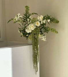 a vase filled with white flowers sitting on top of a table next to a wall