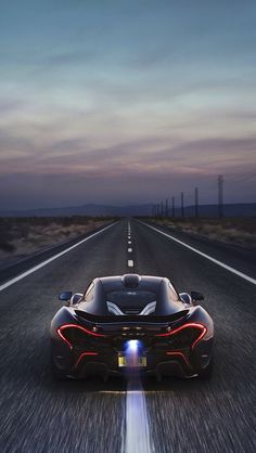 a black sports car driving down an empty road at night with the sun shining on it