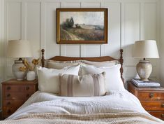 a bed with white linens and pillows in a bedroom next to a painting on the wall