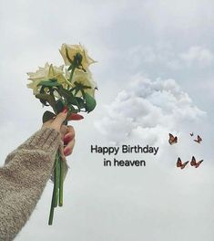 a person holding flowers in front of a sky with butterflies flying around them and the words happy birthday in heaven