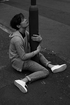 a young man sitting on the ground next to a street pole and holding onto it