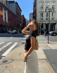 a woman standing on the side of a street next to a cross walk with buildings in the background