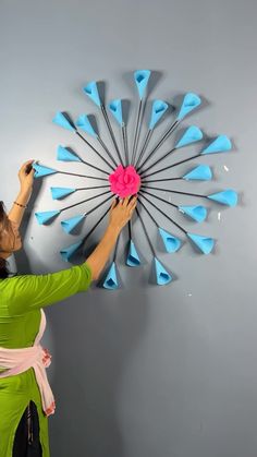 a woman is working on a wall decoration with blue and pink paper flowers in the shape of arrows