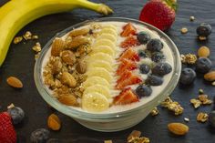 a bowl filled with yogurt, fruit and nuts next to a banana on a table