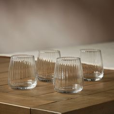 four glasses sitting on top of a wooden table next to each other and one is empty