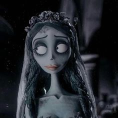 a creepy doll with long hair wearing a tiara and looking at the camera while standing in a dark room