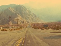 an empty road in the desert with mountains and telephone poles on either side that lead into the distance