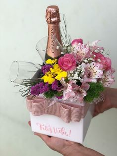 a person holding a box with flowers and a bottle in it