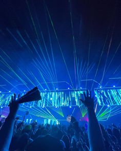 a crowd at a concert with their hands in the air and lights shining down on them