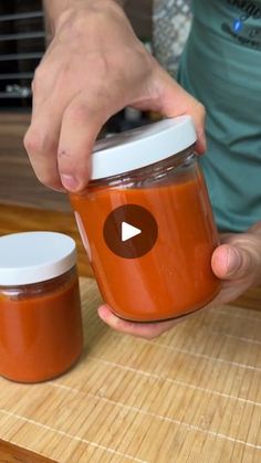 a person is holding a jar with something in it on a wooden table next to two jars