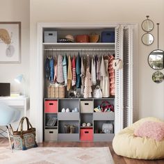 an organized closet with clothes hanging on the rack and storage bins in front of it