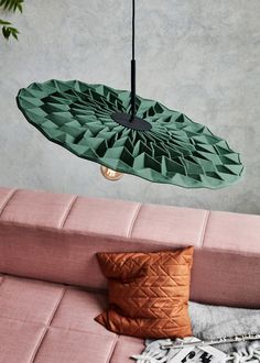 a green umbrella hanging from the ceiling over a pink couch