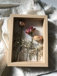 three dried flowers in a wooden frame on a bed