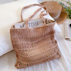 a straw bag sitting on top of a bed next to a hat and book case