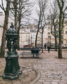 a park with benches, trees and people walking around