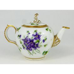 a white tea pot with purple flowers painted on the side and gold trimmings