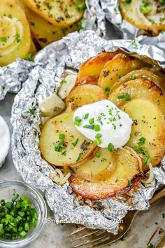 baked potatoes in foil with sour cream and chives on the side, ready to be eaten