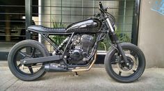 a black motorcycle parked in front of a building next to a plant on the sidewalk