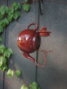 a red teapot hanging from a vine covered wall