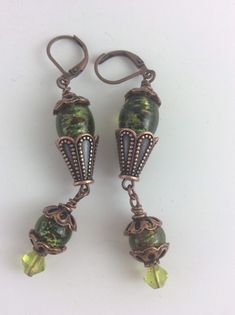 Copper color bead caps and copper lever backs give style to these earrings. The larger beads are lovely lamp work, green with colored speckles. The smaller bead is a green glass bicone crystal. Unique Green Czech Glass Earrings, Unique Green Czech Glass Beaded Earrings, Green Vintage Copper Jewelry, Vintage Green Copper Jewelry, Green Czech Glass Drop Earrings, Vintage Green Czech Glass Earrings, Elegant Green Copper Earrings, Green Czech Glass Beaded Earrings, Wire Wrapped, Green Wire Wrapped Czech Glass Beaded Earrings