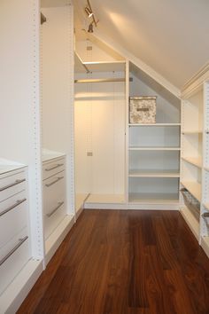 an empty walk in closet with white shelving and wood flooring on the side