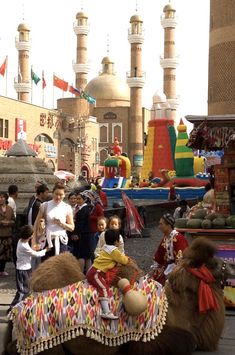 a group of people standing around a camel in the middle of a street filled with children