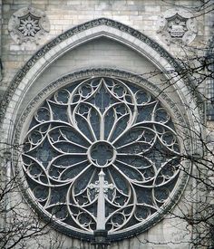 an ornate window on the side of a building with trees around it and branches in front of it