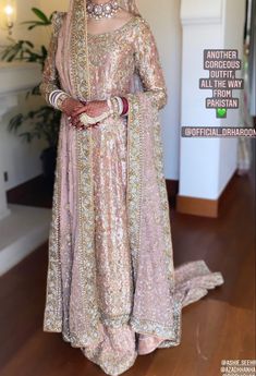 a woman in a pink and gold wedding outfit standing on a wooden floor with her hands behind her head