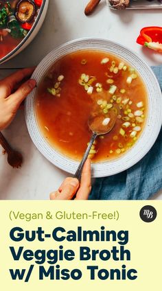 a person holding a spoon over a bowl of vegetable broth with the title vegan & gluten - free gutt - calming veggie broth w / miso tonic