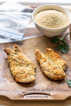 two pieces of fried chicken on a cutting board next to a bowl of seasoning