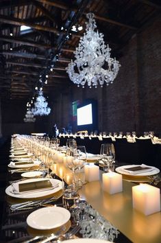 a long table is set with white plates and silverware, candles and chandelier