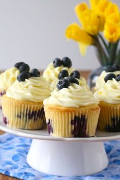 cupcakes with blueberries and cream frosting on a plate next to yellow flowers