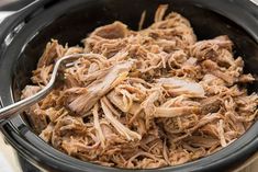 shredded pulled pork in a slow cooker with a ladle resting on the side