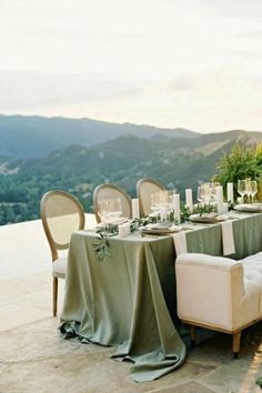 a table set up with place settings and greenery on it for an outdoor dinner