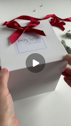 a person opening a white gift box with red ribbon