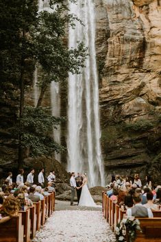 a bride and groom standing in front of a waterfall at their outdoor wedding ceremony with guests seated on the pews