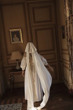 a woman in a white dress and veil walking through a room with a painting on the wall