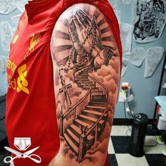 a man wearing a red shirt and holding his hands up to the sky with a stairway tattoo on his arm