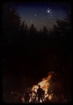 a man standing in front of a campfire at night with the stars above him