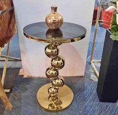 a glass table with gold balls on it and a vase in the back ground behind it