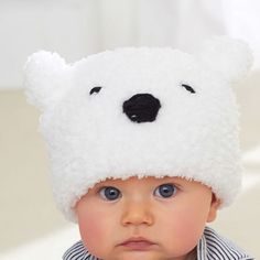 a baby wearing a white bear hat on top of it's head and looking at the camera