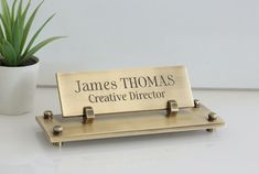 a desk with a sign that says james thomas creative director on it and a potted plant in the background