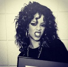 a black and white photo of a woman with curly hair holding a sign in front of her face