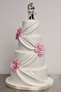 a white wedding cake with pink flowers and a bride and groom figurine on top