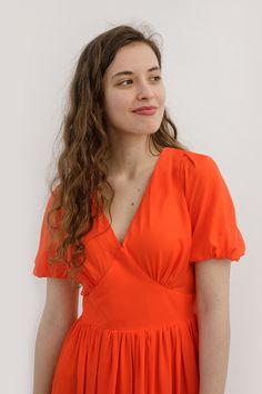 a young woman in an orange dress poses for a photo against a white background with her long hair pulled back